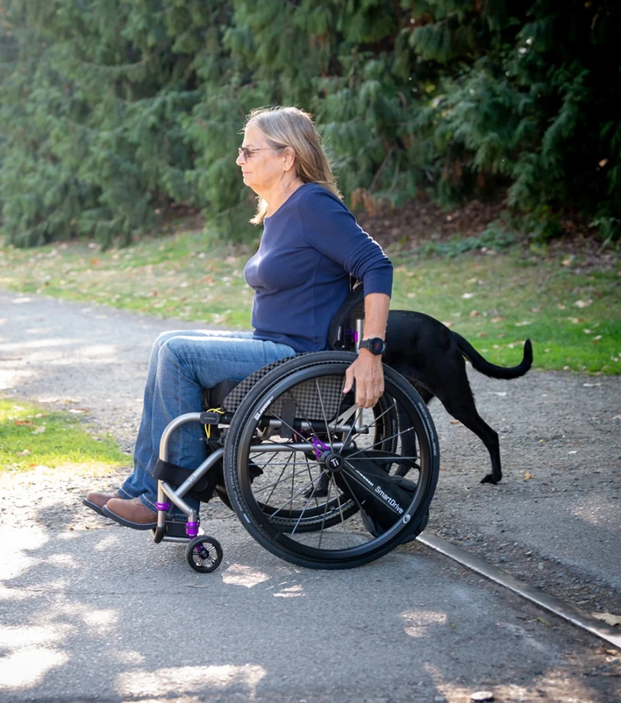 Side image of a woman utilizing the SmartDrive MX2+ Switch Control - Joystick controller for powered wheelchairs, designed for users with limited mobility to operate through switch controls.