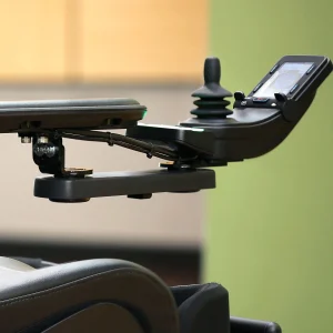 Back view of the Retractable Joystick Mount on wheelchair. A sleek, metal joystick mount attached to a wheelchair armrest. The joystick can be easily swung outwards or retracted sideways for improved accessibility.